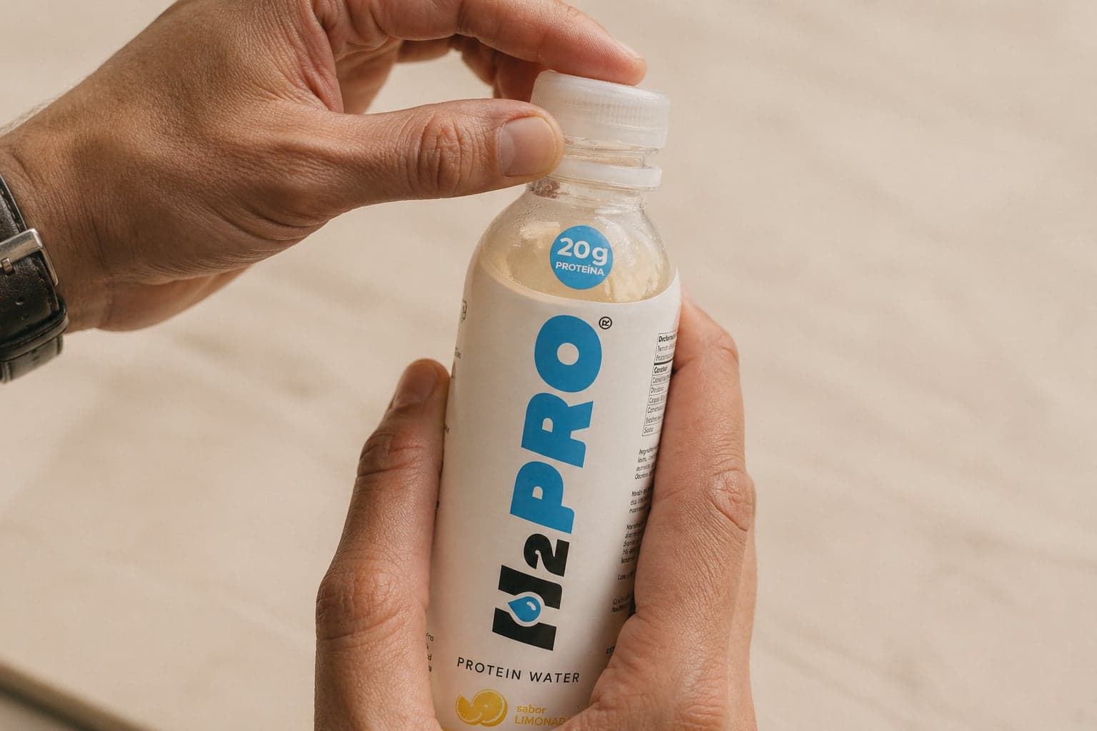 Manos abriendo la tapa de una botella H2PRO — una vuelta y lista para tomar